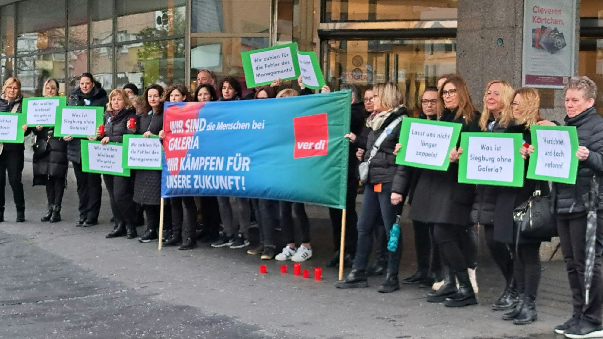 Männer und Frauen mit einem Banner stehen vor dem Siegburger Kaufhof.