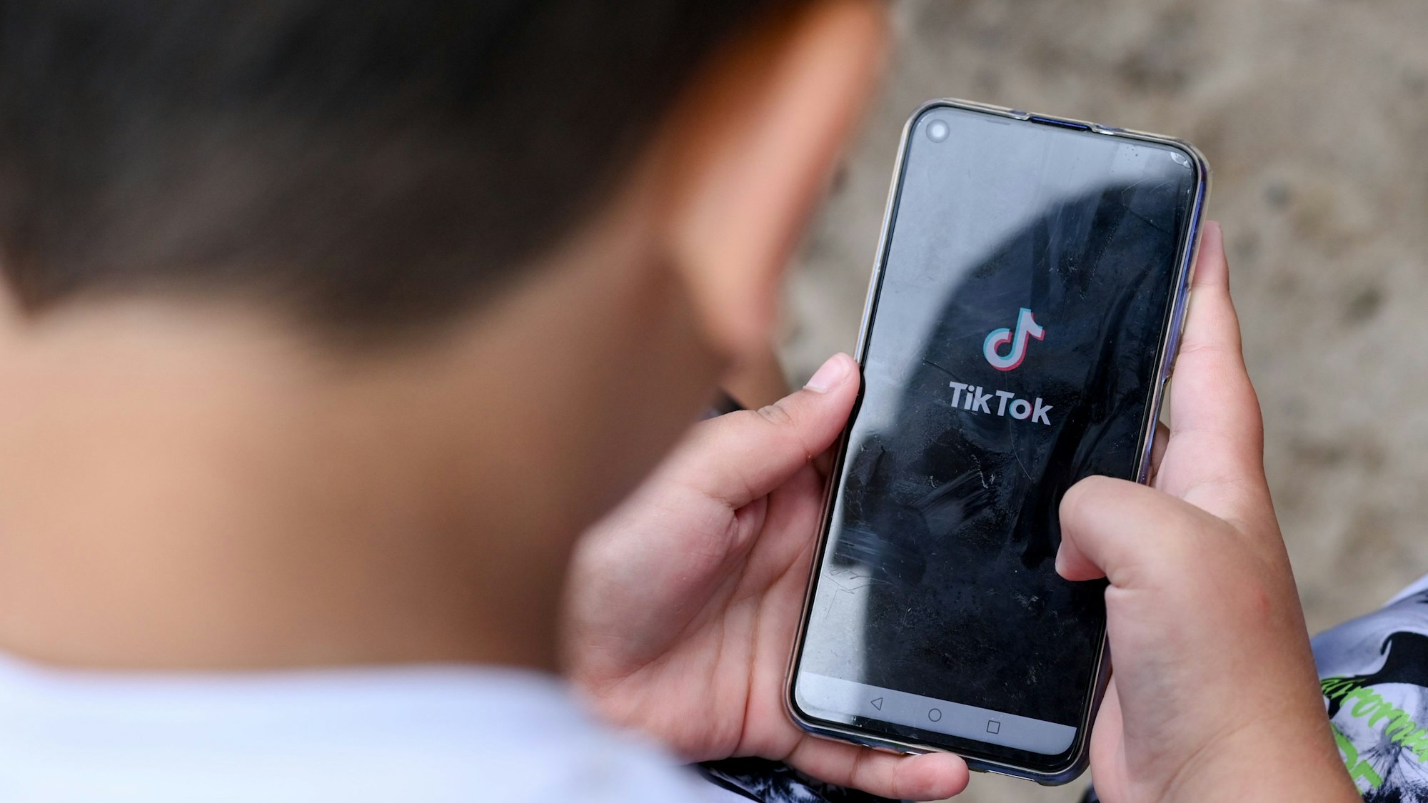 Ein Junge hält ein Smartphone in den Händen, auf dem das Logo der Kurzvideo-App TikTok zu sehen ist. (Symbolbild)