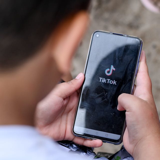Ein Junge hält ein Smartphone in den Händen, auf dem das Logo der Kurzvideo-App TikTok zu sehen ist. (Symbolbild)