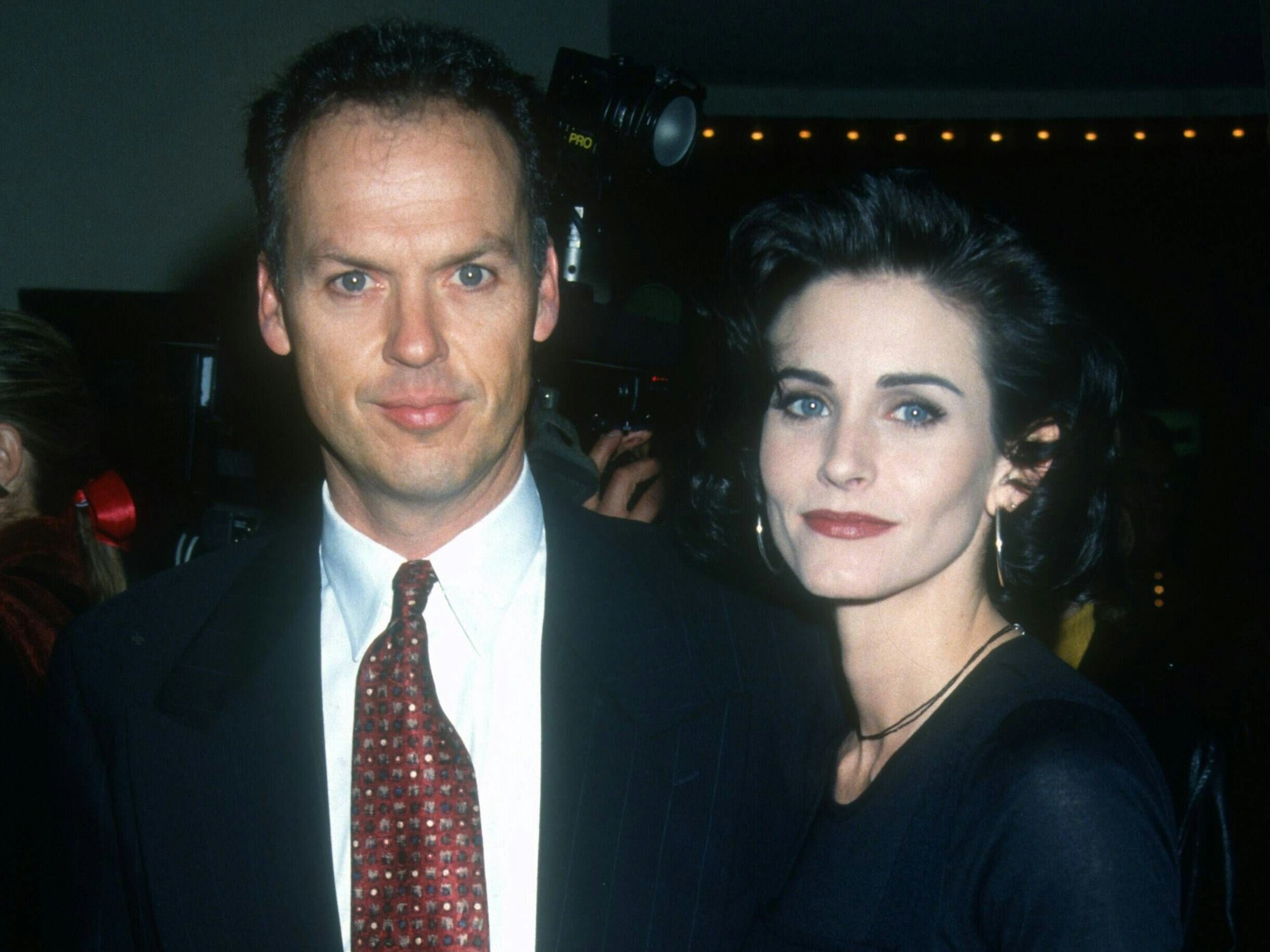 Das Foto zeigt die Schauspieler Michael Keaton und Courteney Cox, die lächelnd für ein Foto posieren. Der Aufnahmeort ist unbekannt.