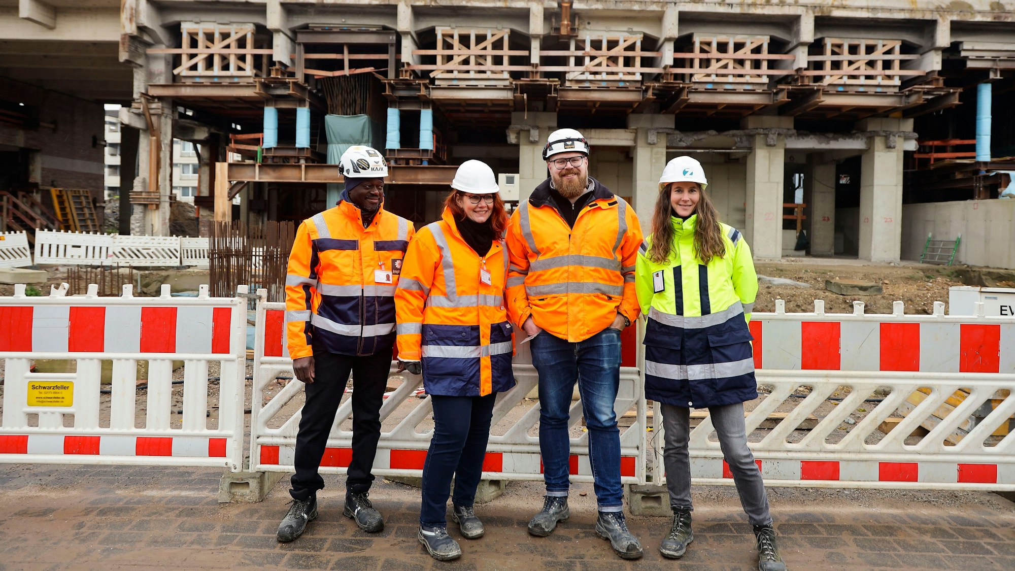 Haroumaa Ourdraogo, Sonja Rode,Christian Nolting und Sonja Naeckel (von links) stehen auf der Baustelle vor einer Absperrung und Betonbauteilen.