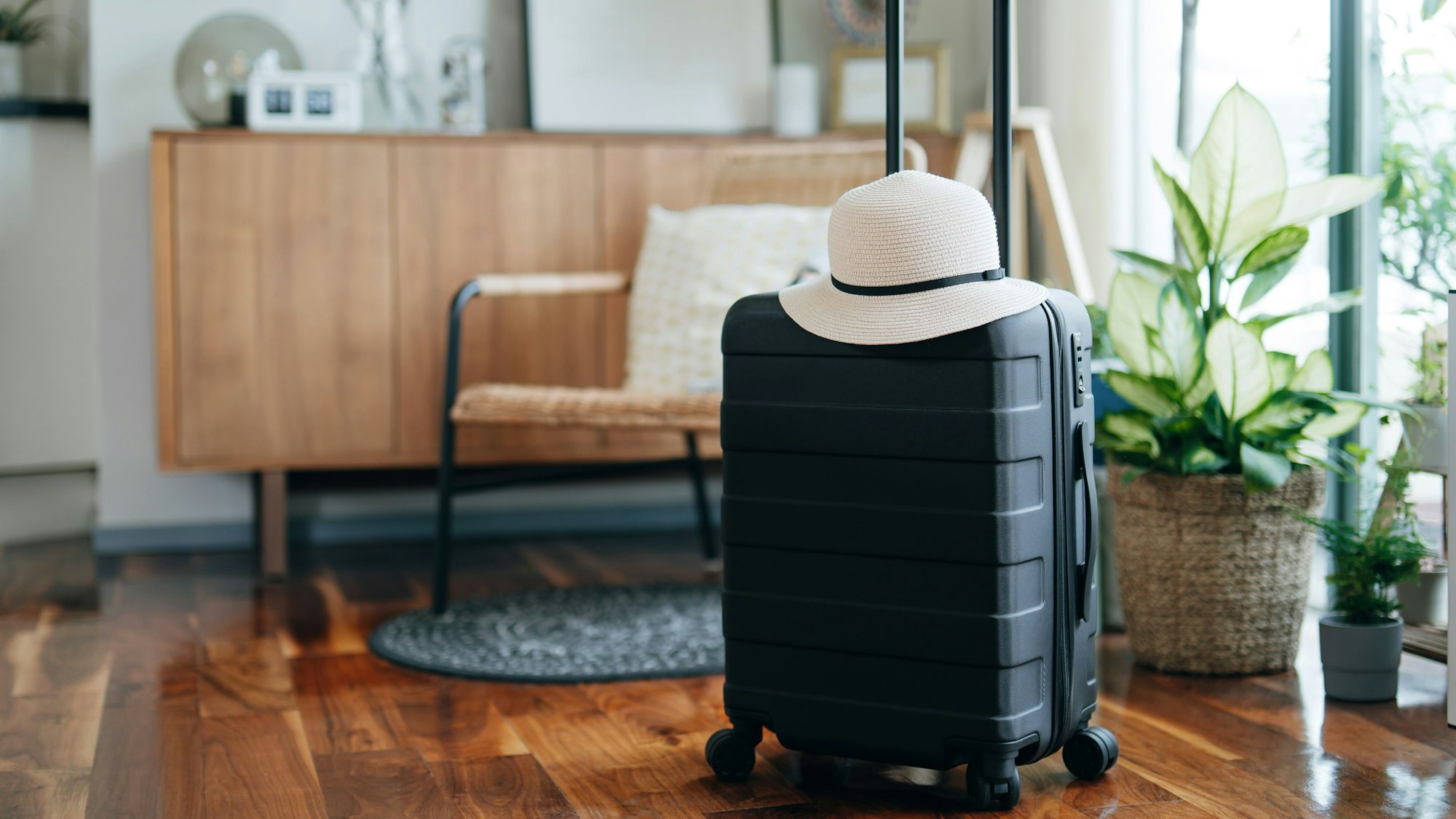 In einem Wohnzimmer steht ein kleiner schwarzer Koffer, darauf liegt ein weißer Hut