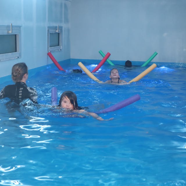 Kinder schwimmen mithilfe von Poolnudeln in einem mobilen Schwimmcontainer.