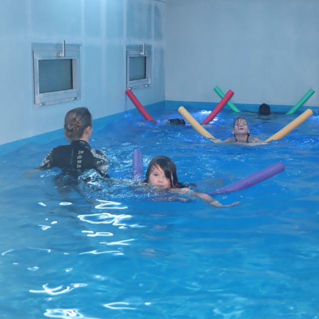 Kinder schwimmen mithilfe von Poolnudeln in einem mobilen Schwimmcontainer.