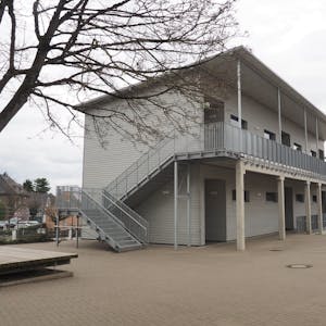 Das Foto zeigt ein graues zweigeschossiges Gebäude mit Außentreppe.