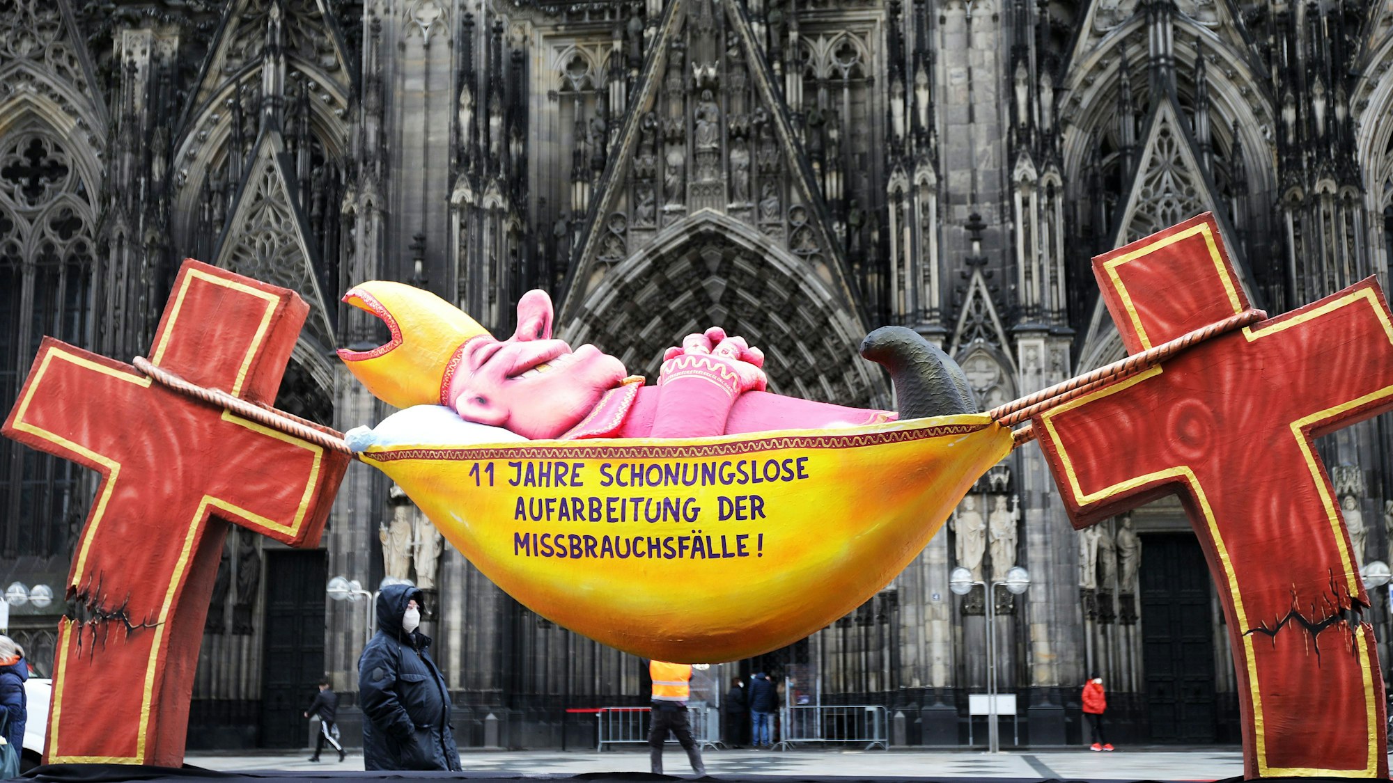 Mit einer satirischen Plastik, aufgestellt vor dem Kölner Dom, wirft der Künstler Jacques Tilly der katholischen Kirche mangelnde Bereitschaft zur Aufarbeitung des Missbrauchsskandals vor.