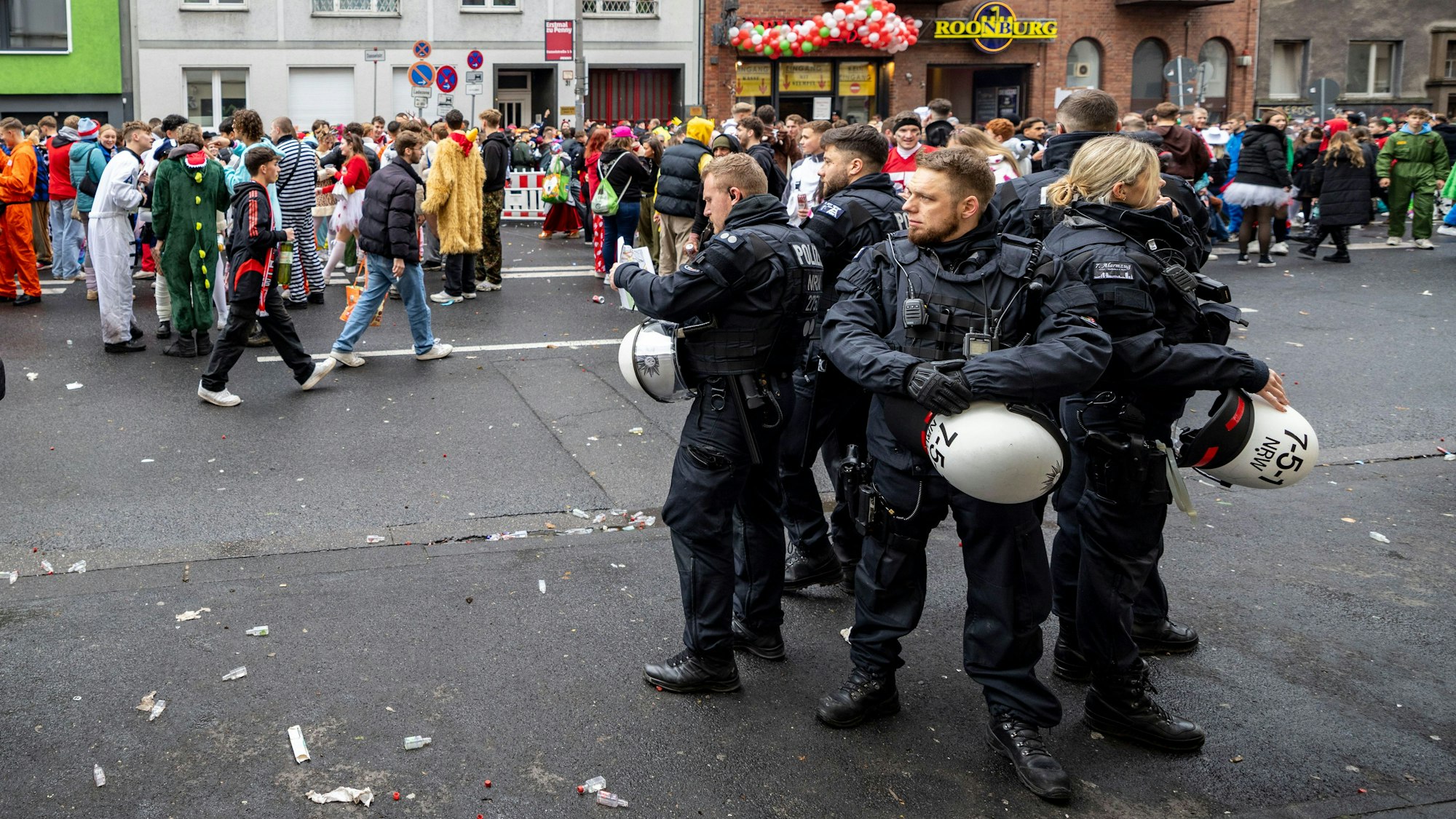 Polizeibeamte stehen auf der Zülpicher Straße, hinter ihnen laufen Kostümierte.