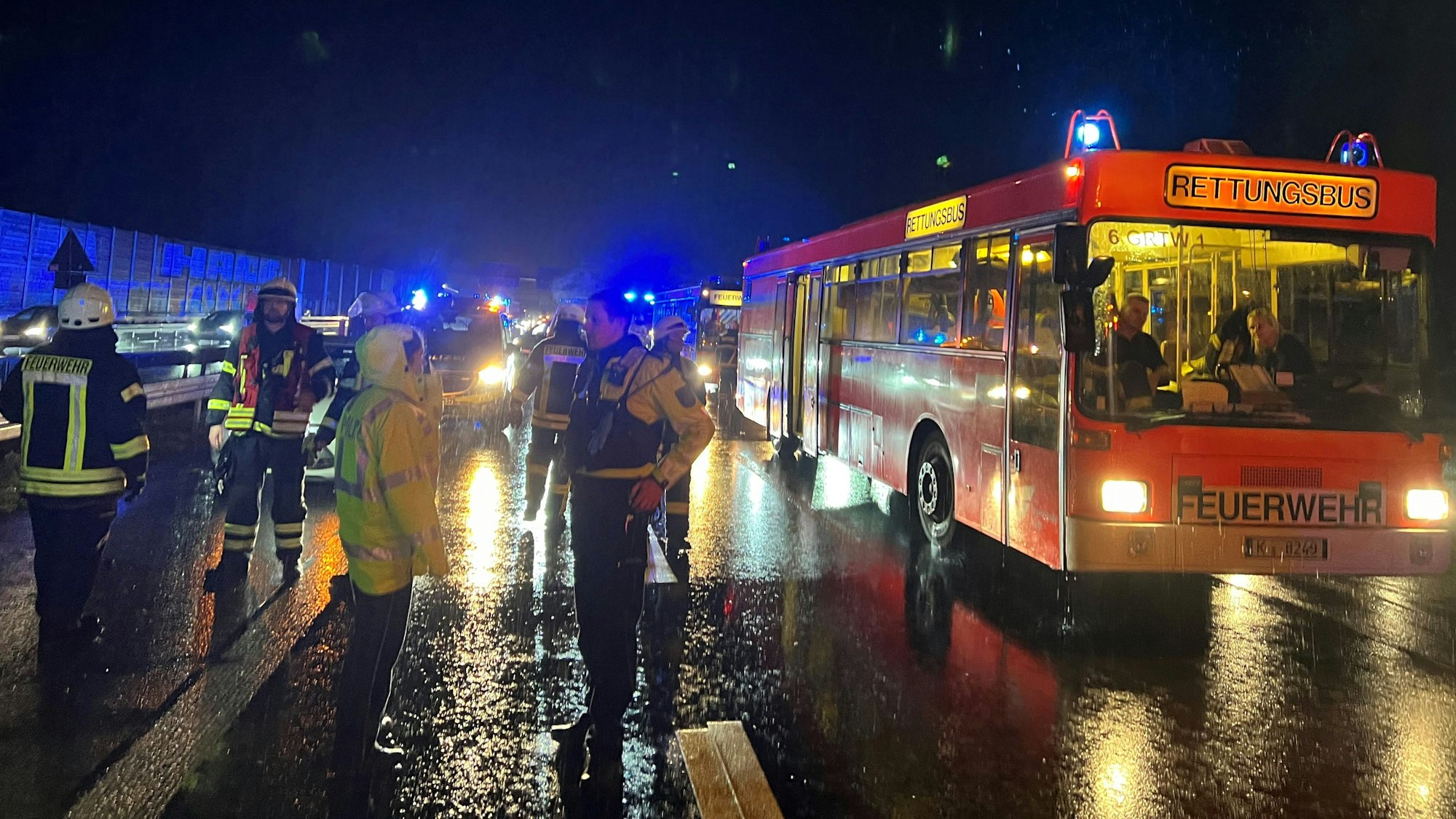Das Bild zeigt einen Rettungsbus der Feuerwehr und mehrere Einsatzkräfte der Feuerwehr und Polizei bei strömenden Regen.