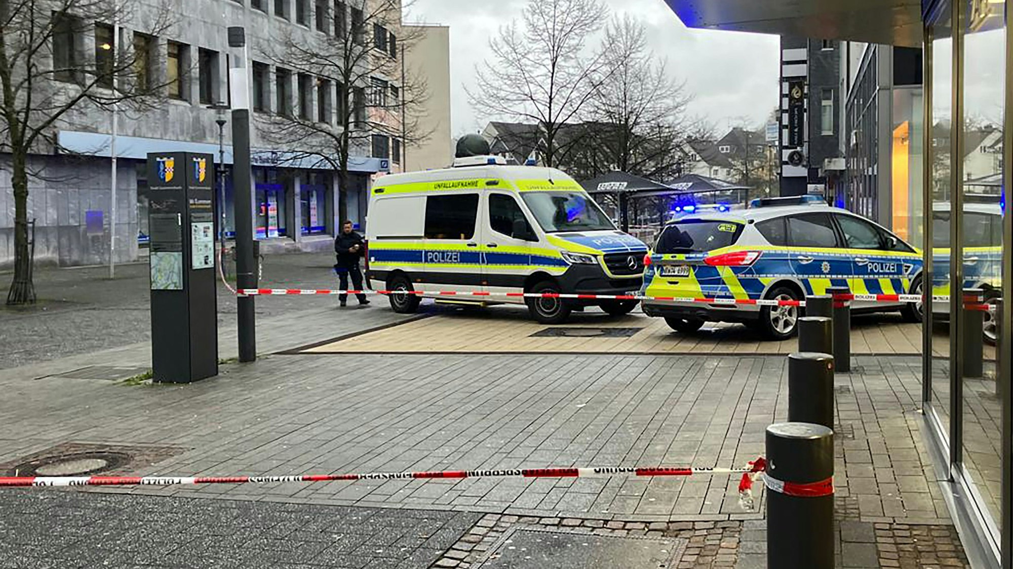 Zwei Polizeiwagen stehen in der Gummersbacher Innenstadt. Um ein Geschäft ist eine Fläche mit Flatterband abgesperrt.