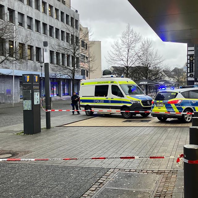 Zwei Polizeiwagen stehen in der Gummersbacher Innenstadt. Um ein Geschäft ist eine Fläche mit Flatterband abgesperrt.