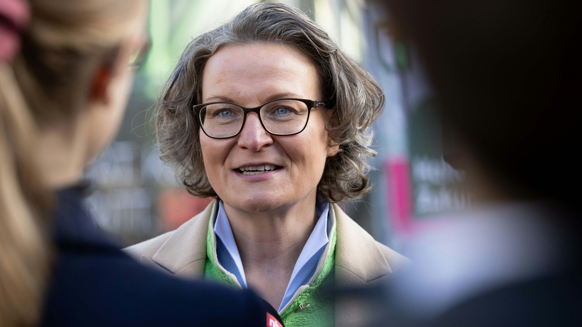 Ina Scharrenbach (CDU), Heimatministerin von Nordrhein-Westfalen, ist während eines Baustellenbesuchs im Porträt zu sehen. Sie trägt einen beigen Mantel und ein buntes Halstuch.