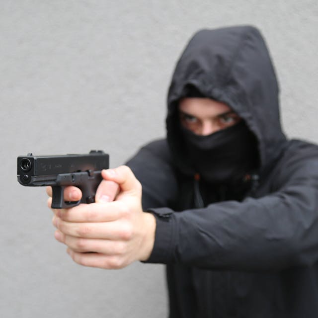 In einer gestellten Szene droht ein maskierter Mann mit einer Schusswaffe.