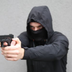 In einer gestellten Szene droht ein maskierter Mann mit einer Schusswaffe.