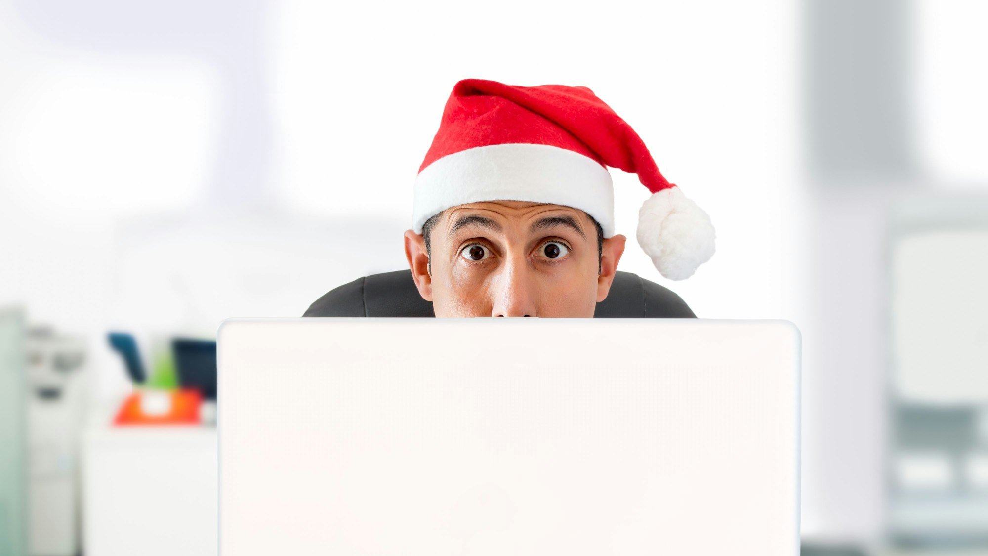 Junger Mann mit Nikolausmütze bestellt Weihnachtsgeschenke im Internet