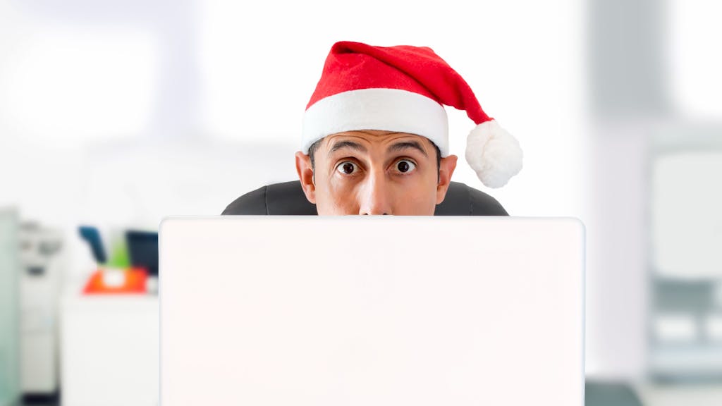 Junger Mann mit Nikolausmütze bestellt Weihnachtsgeschenke im Internet