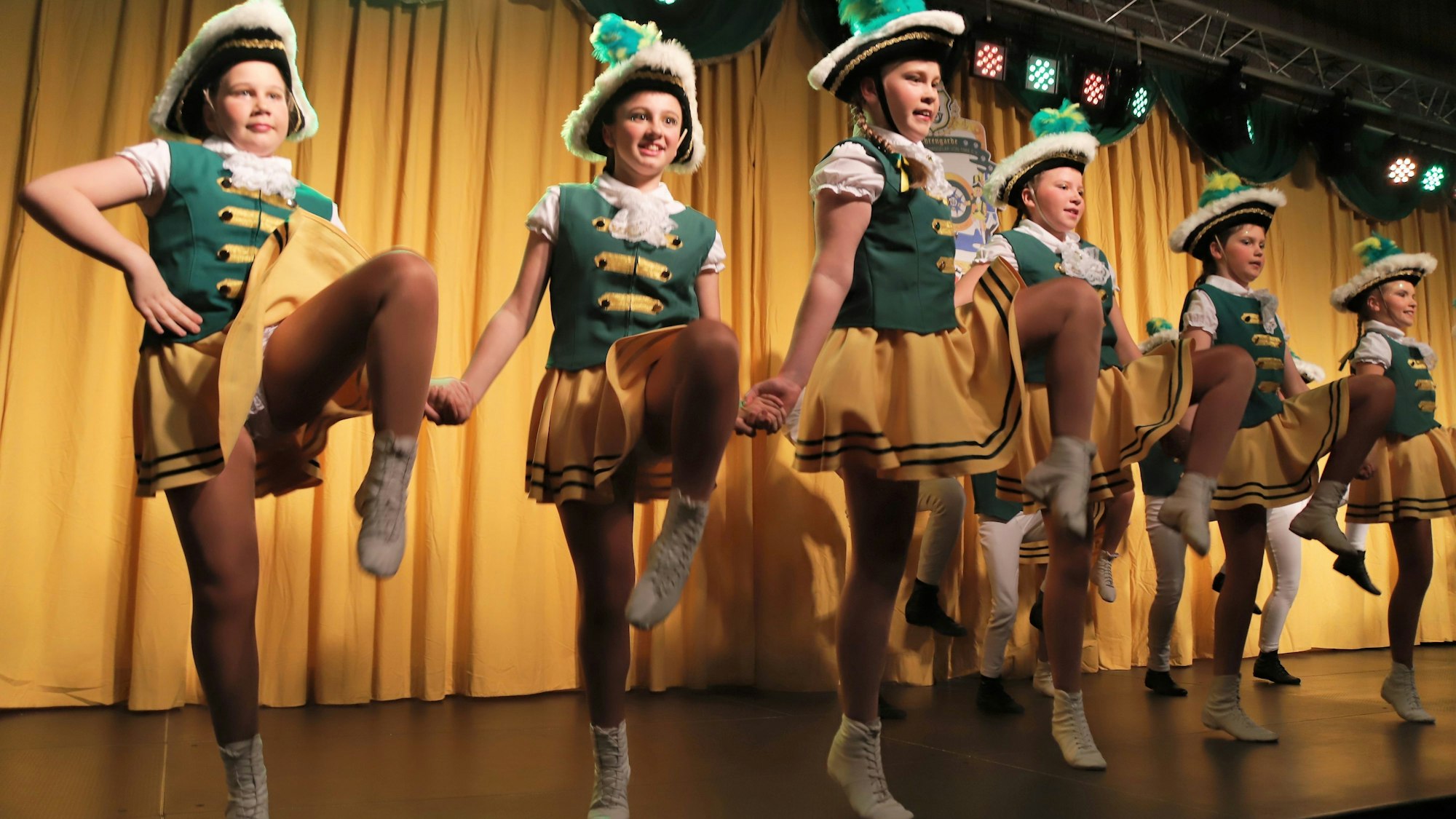 Tanzmariechen in grün-goldenen Kostümen auf einer Bühne.