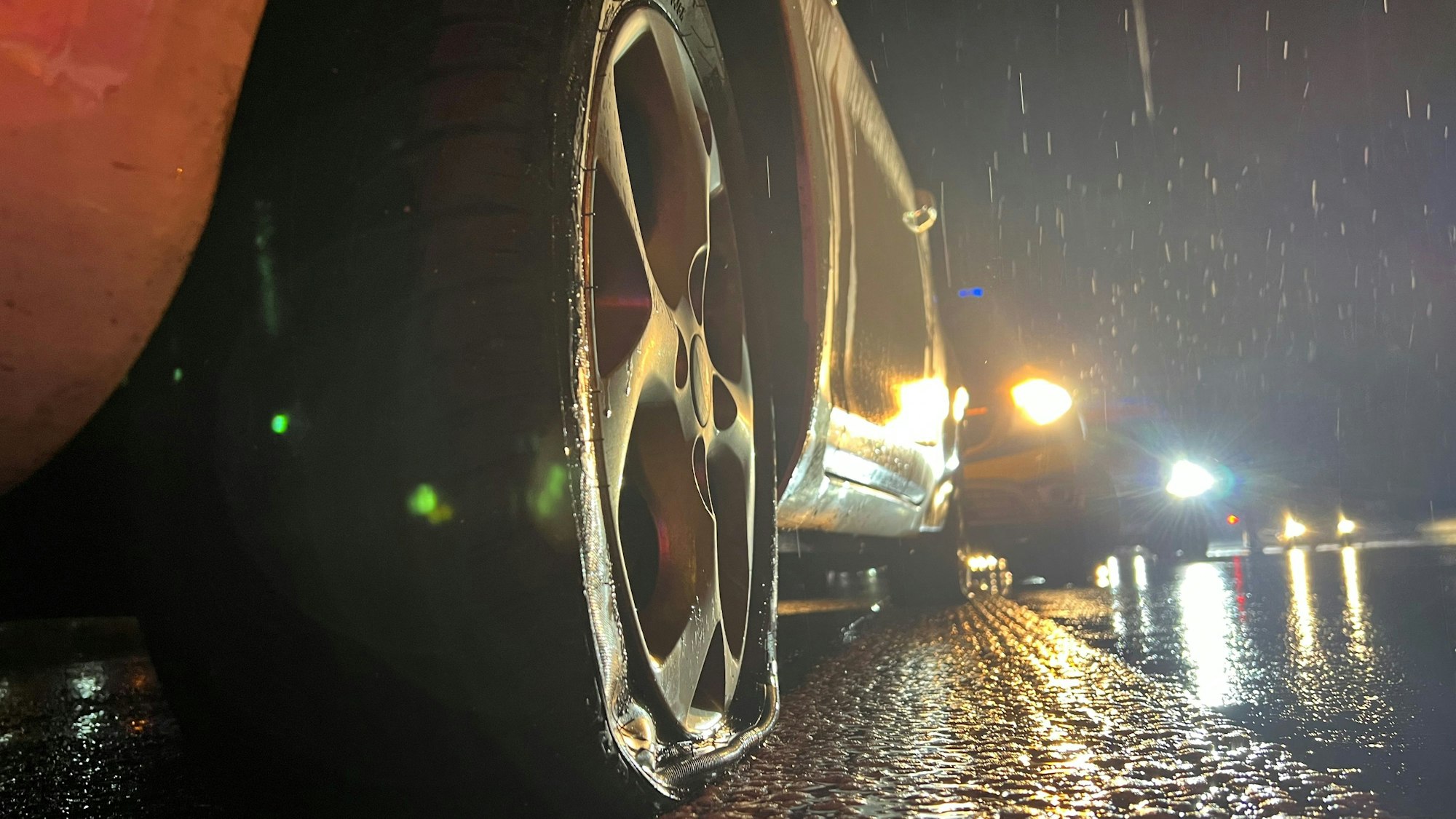 Das Bild zeigt einen platten Reifen an einem Auto. Das Fahrzeug steht bei strömenden Regen auf der Autobahn.