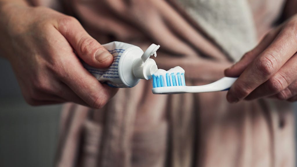 Auf dem Foto drückt ein Mann Zahnpasta aus der Tube auf seine Zahnbürste.