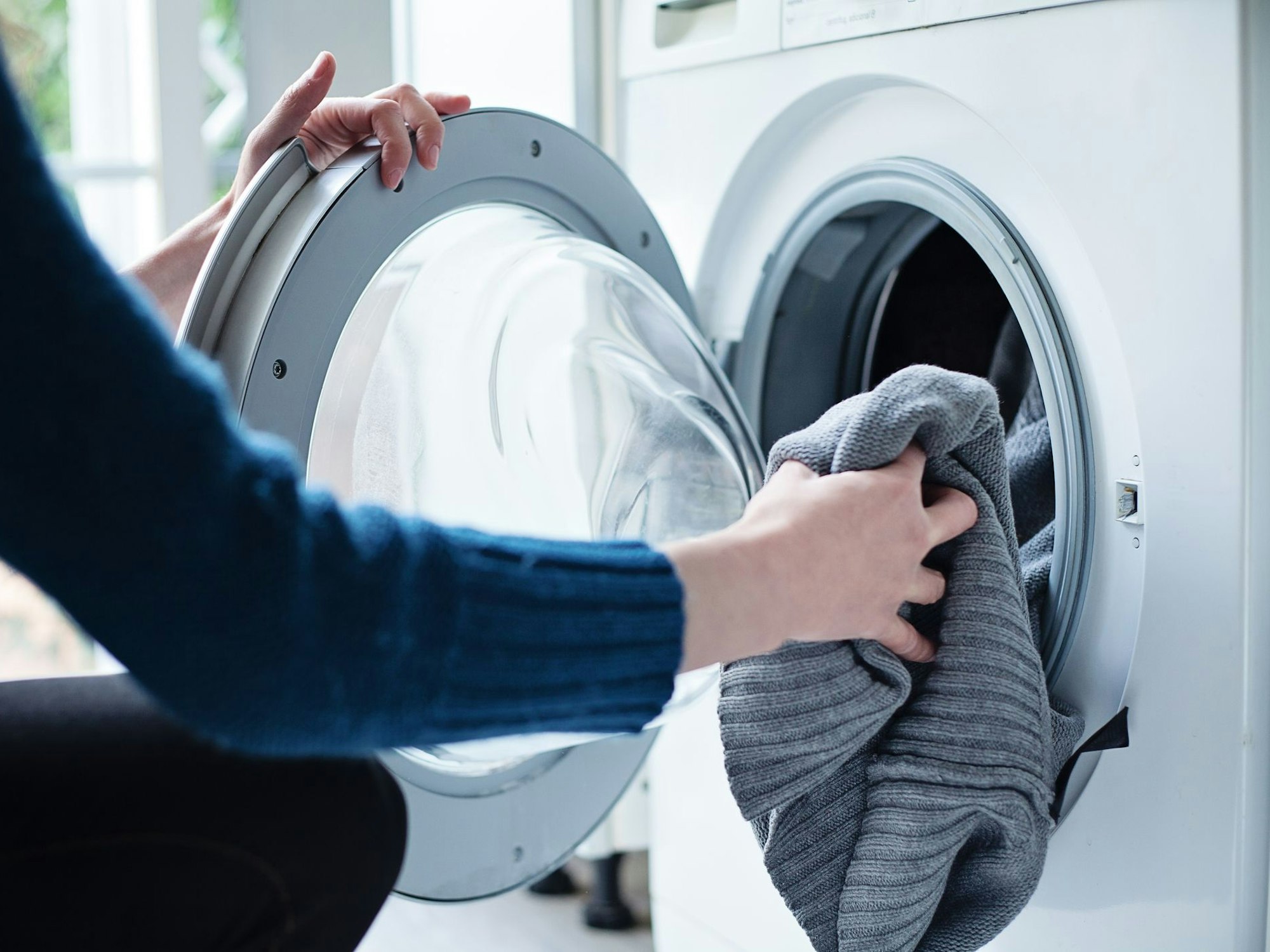 Auf dem Foto befüllt eine Frau eine Waschmaschine mit Wäsche.