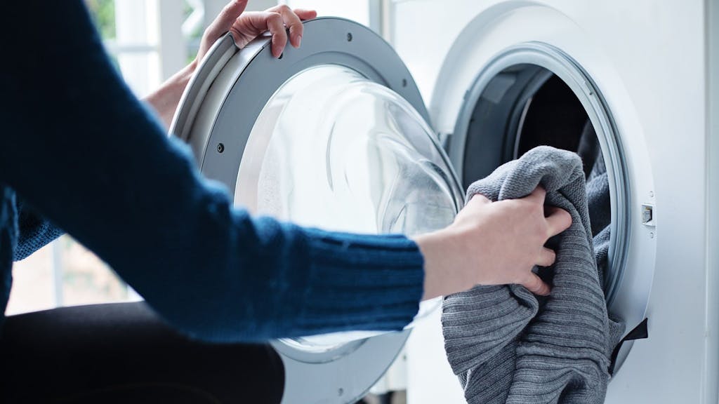 Auf dem Foto befüllt eine Frau eine Waschmaschine mit Wäsche.&nbsp;