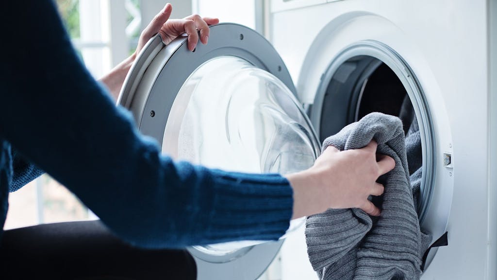 Auf dem Foto befüllt eine Frau eine Waschmaschine mit Wäsche.&nbsp;