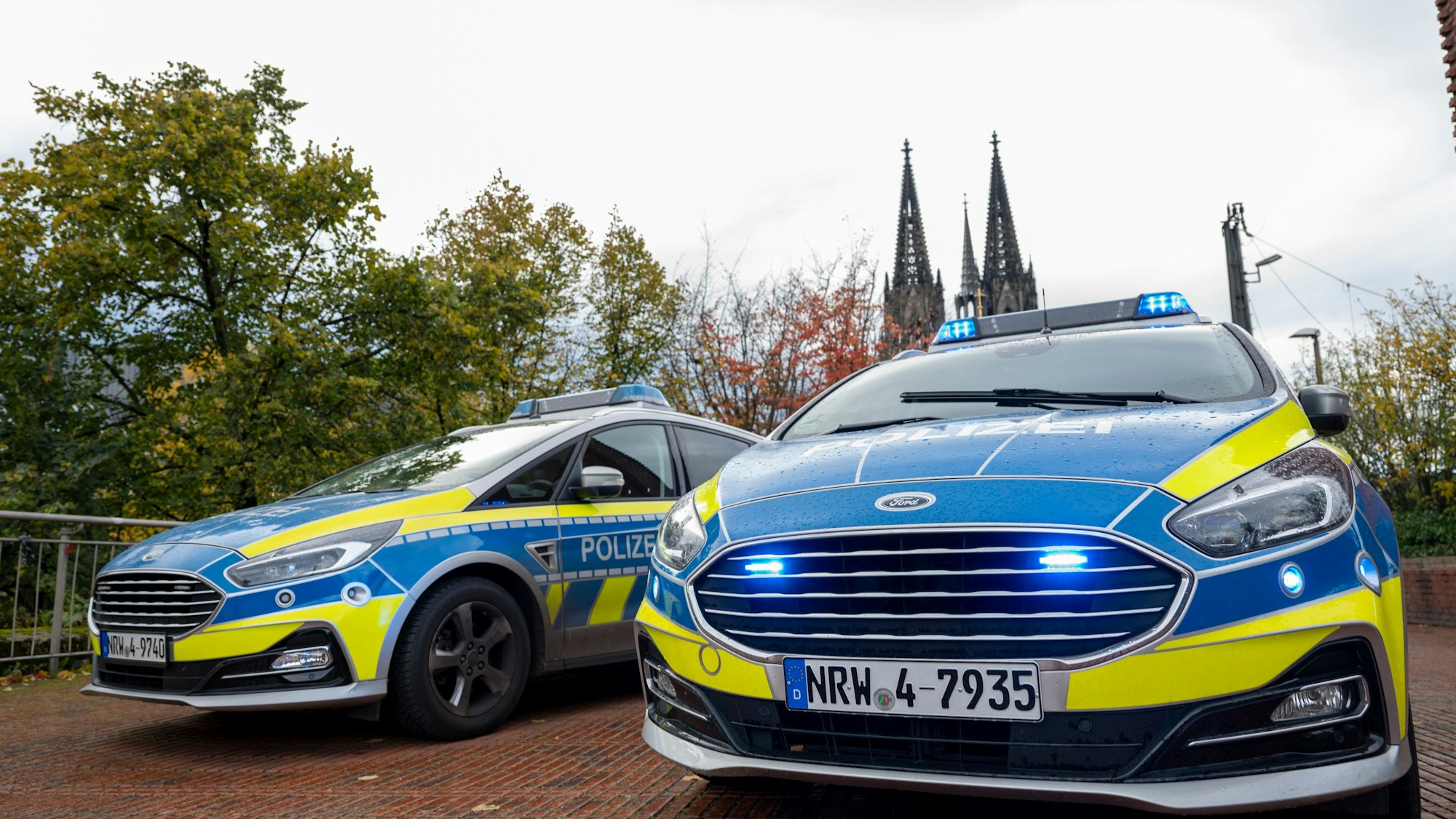 Zwei Polizeiwagen mit Blaulicht, im Hintergrund ist der Kölner Dom zu sehen.