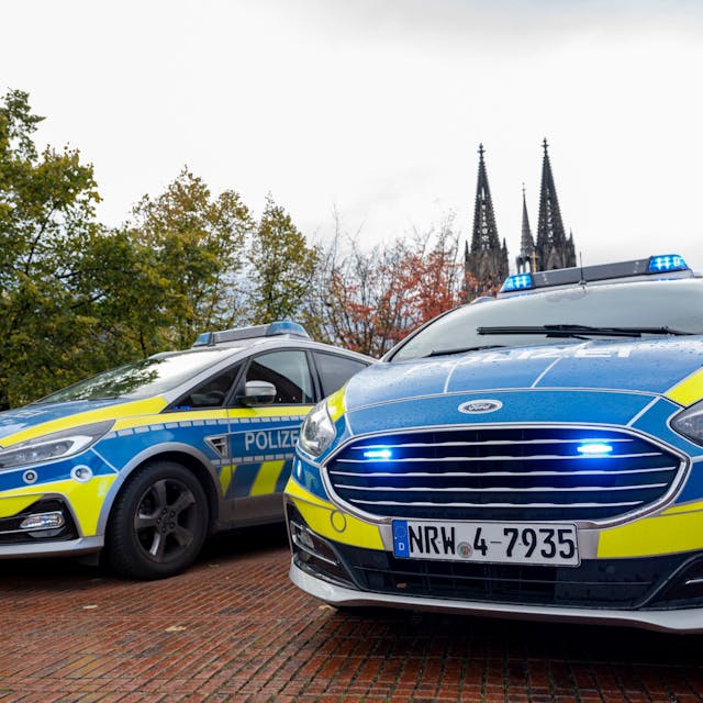 Zwei Polizeiwagen mit Blaulicht, im Hintergrund ist der Kölner Dom zu sehen.