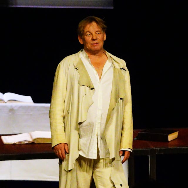 Ein Mann steht in heller, weiter Kleidung auf einer Bühne.