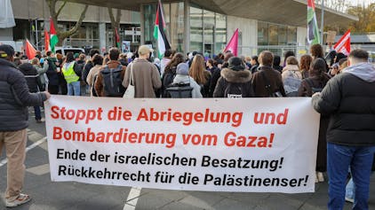 Demonstrierende stehen vor dem Hauptgebäude der Uni Köln mit einem Plakat mit der Aufschrift „Stoppt die Abriegelung und Bombardierung vom Gaza“.