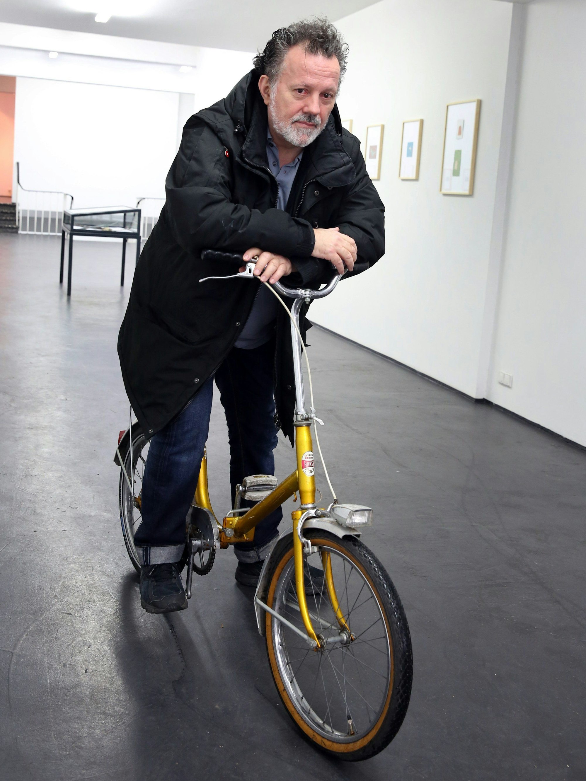 Der Künstler Walter Dahn posiert auf einem gelben Fahrrad.