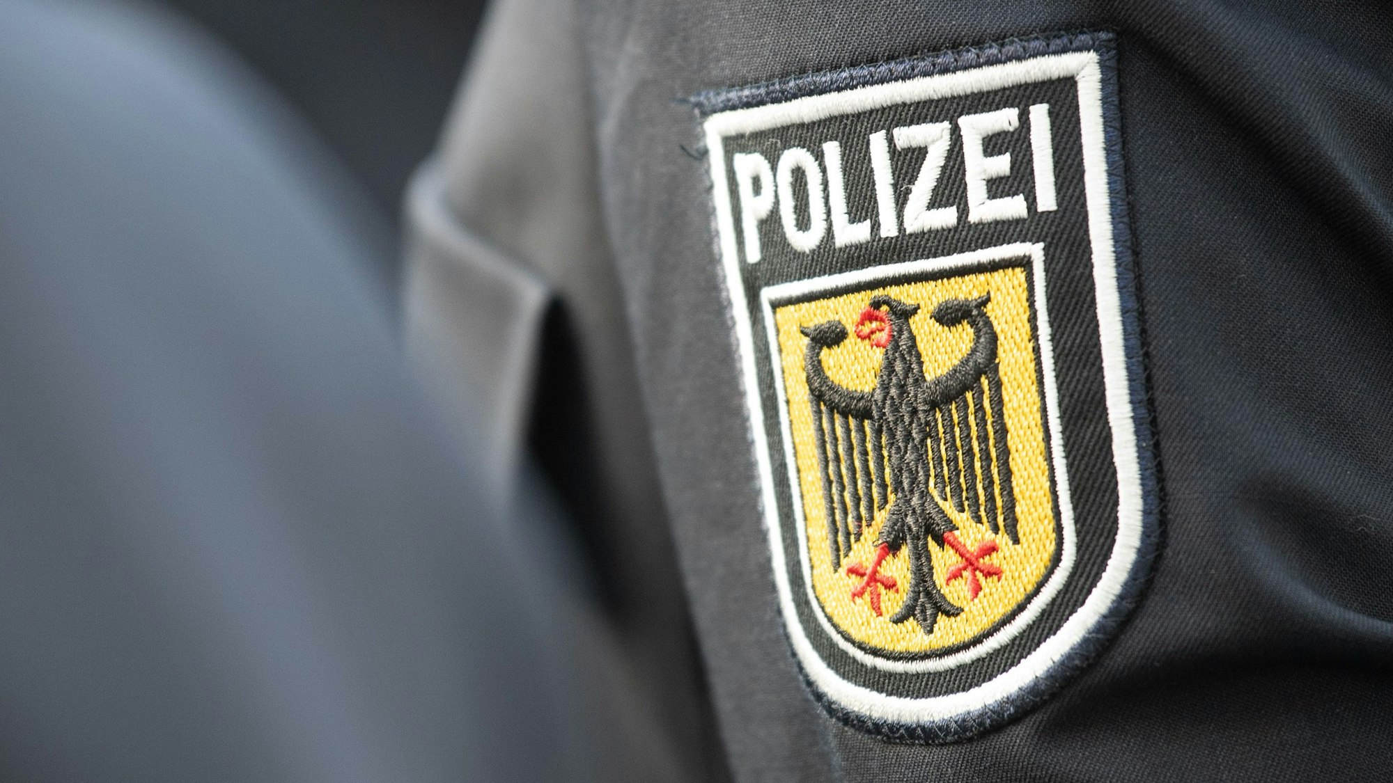 Junge Bundespolizistinnen und Polizisten stehen bei ihrer Vereidigung im Innenhof der Bundespolizeiinspektion am Flughafen Frankfurt, dabei ist ein Polizeiabzeichen auf einem Ärmel zu sehen.