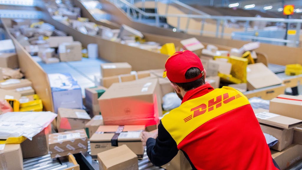 Ein Paketzusteller sortiert und räumt in einer Zustellbasis von Deutsche Post DHL Pakete in ein Zustellfahrzeug.