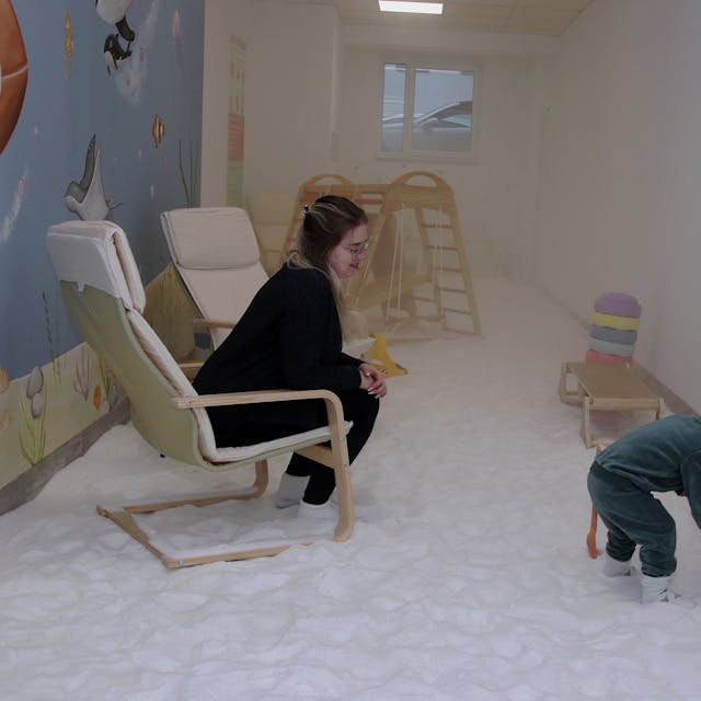 Eine Frau sitzt in einem Sessel, ihr Kind spielt in dem Salzraum.