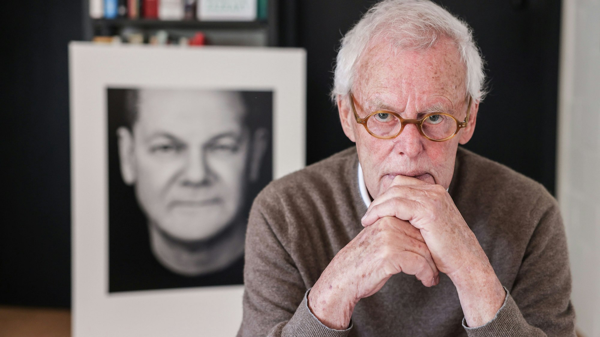 Der Porträtfotograf Konrad Rufus Müller sitzt in seinem Wohnzimmer vor einem Schwarz-Weiß-Porträt von Bundeskanzler Scholz