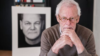 Der Porträtfotograf Konrad Rufus Müller sitzt in seinem Wohnzimmer vor einem Schwarz-Weiß-Porträt von Bundeskanzler Scholz&nbsp;
