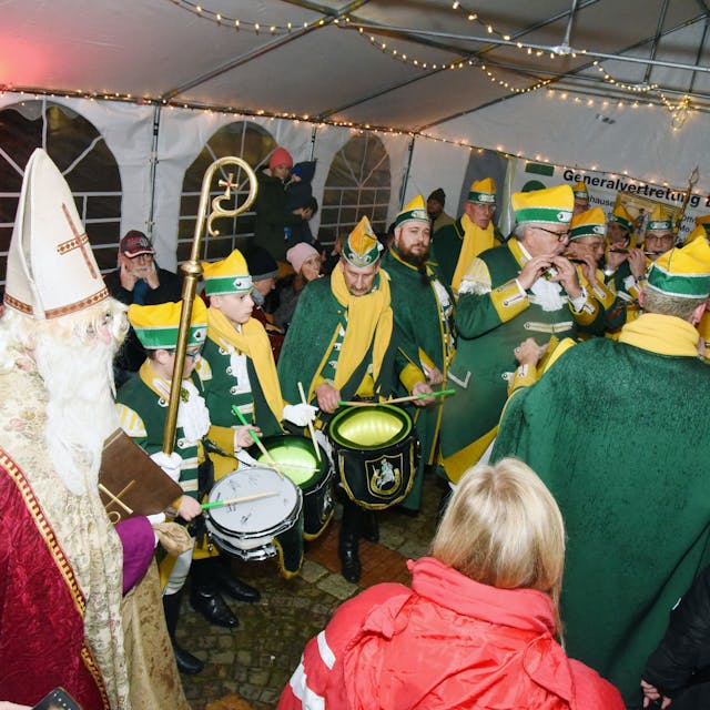 Ein Mann im Nikolaus-Kostüm steht inmitten von Musikern des Spielmannszugs der Ehrengarde in einem weißen Zelt.&nbsp;