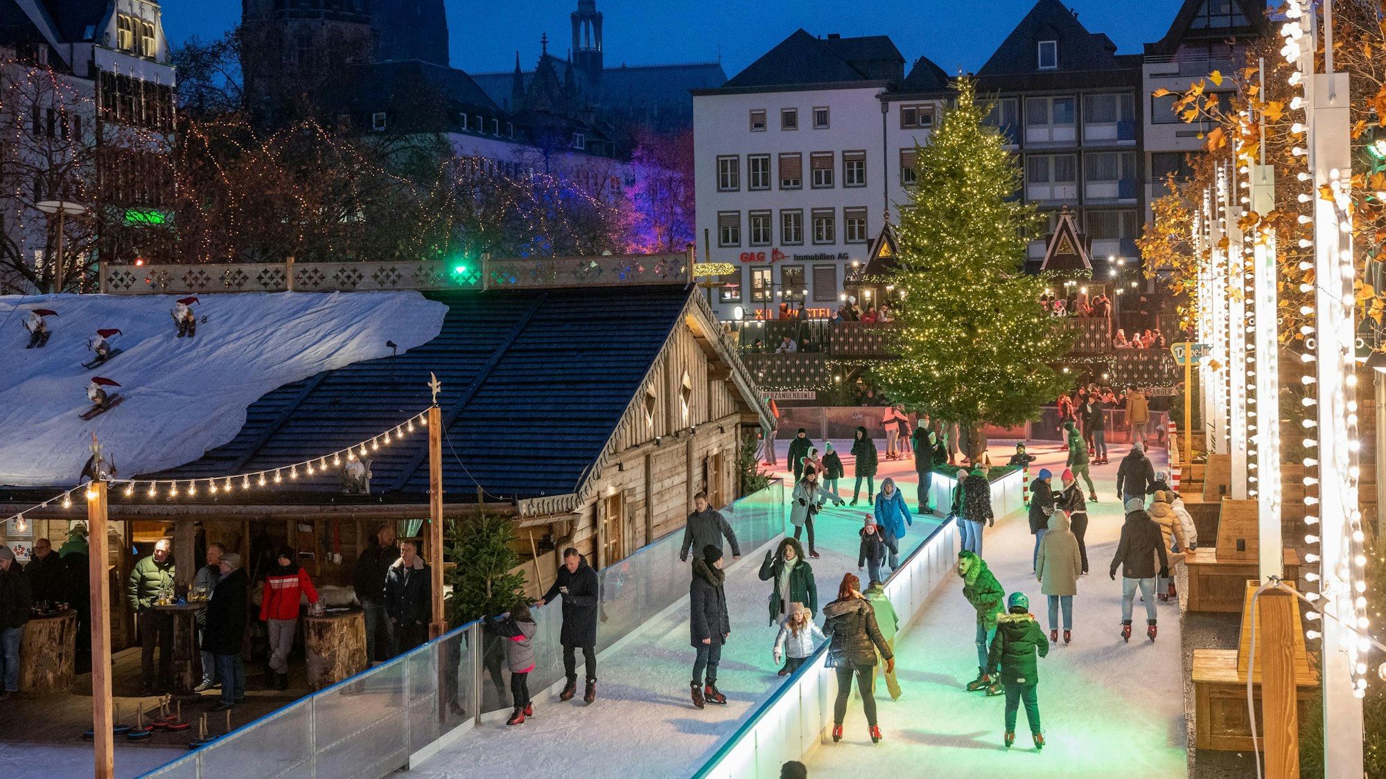 Auf dem Heumarkt ist eine Schlittschuhbahn aufgebaut. Menschen fahren über das Eis. Im Hintergrund ist der Kölner Dom zu erkennen.
