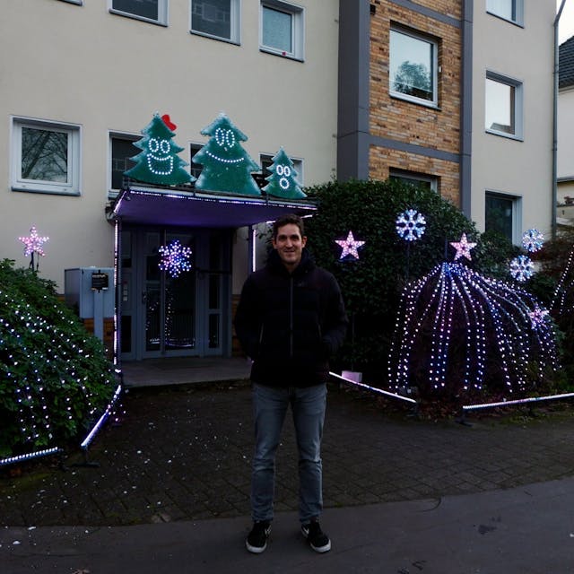 Simon Biela vor dem bunt blinkendem Eingangsbereich seines Wohnhauses.