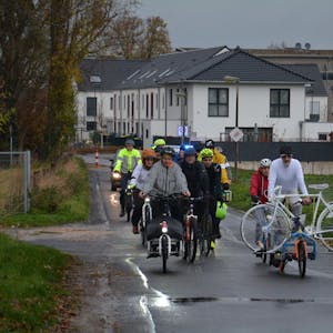 Fahrräder fahren über einen Feldweg, einer transportiert ein weißes Geisterfahrrad.