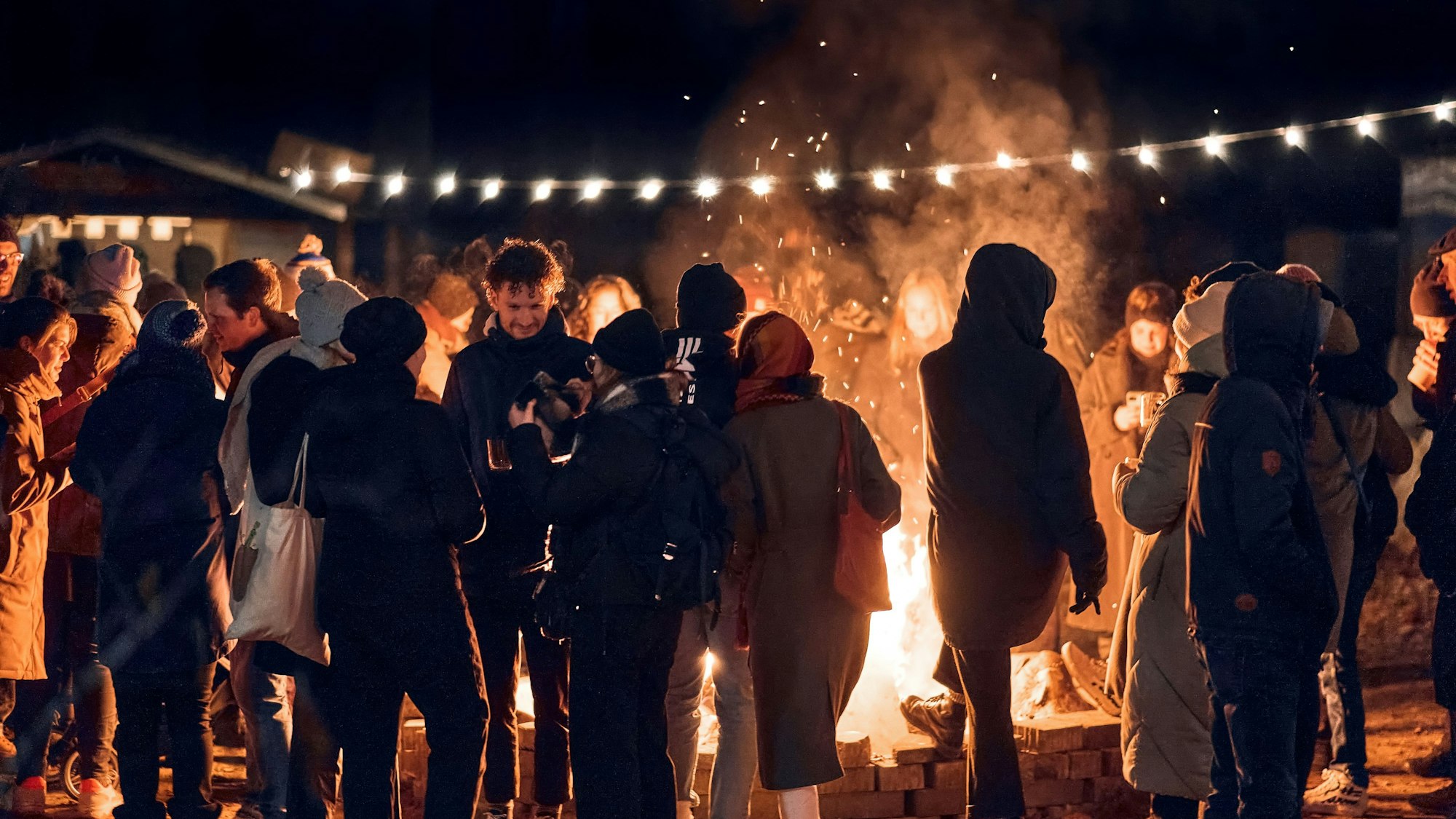 Personen stehen im Dunkeln um das Lagerfeuer auf dem „Veihnachtsmarkt“ herum.