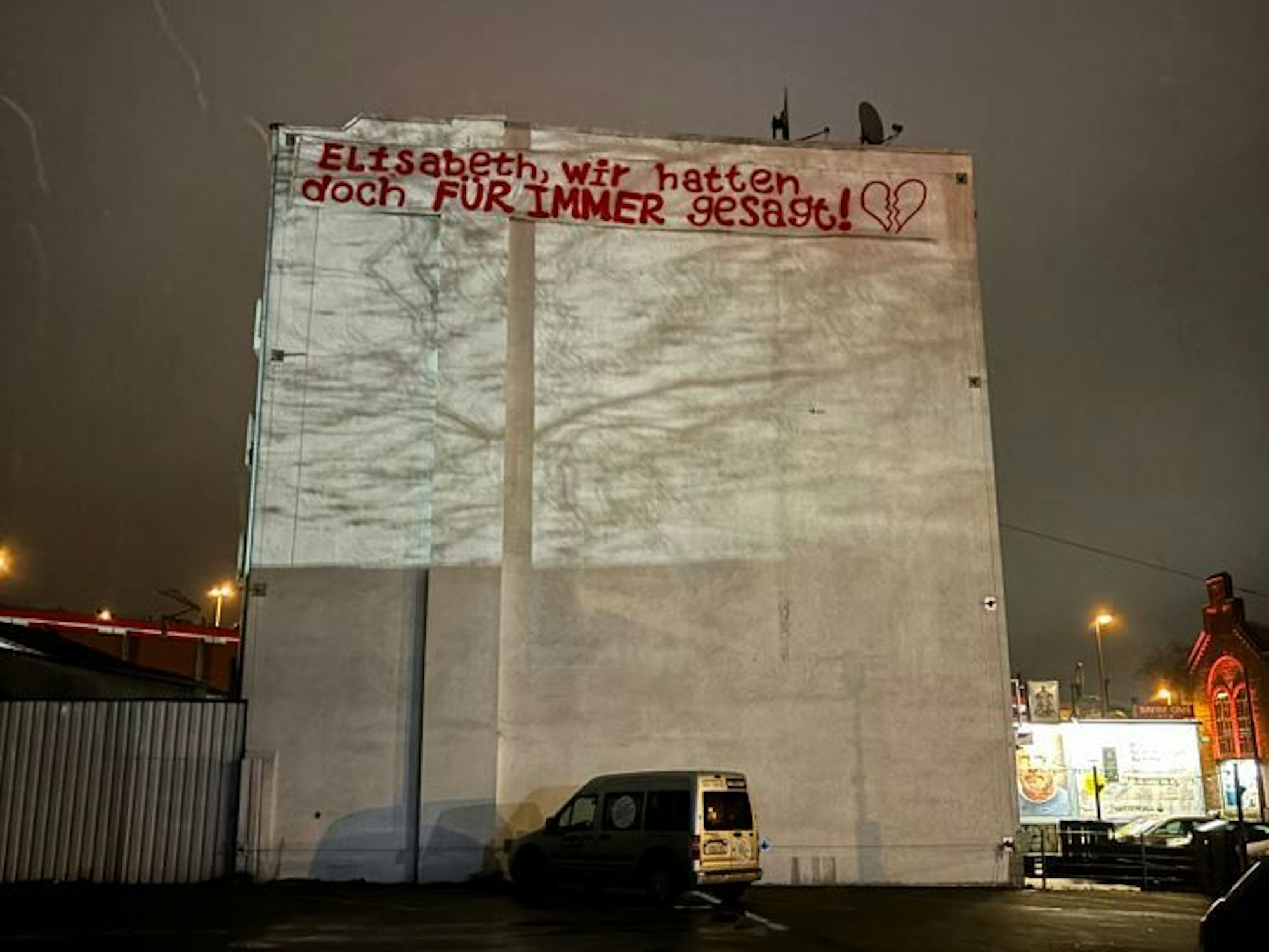 Foto in der Dunkelheit von einer Hausfassade in Köln. Dort hängt ein Plakat.