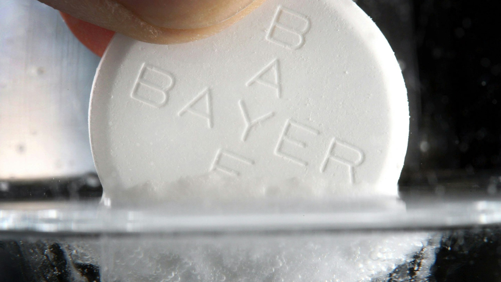 Eine Aspirin-Tablette des Bayer-Konzerns löst sich in einem Wasserglas auf.