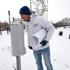 Im Vordergrund schaut Dr. Karsten Brandt in das zylindrische Niederschlagsmessgerät, im Hintergrund das Gerüst der verschneiten Wetterstation.