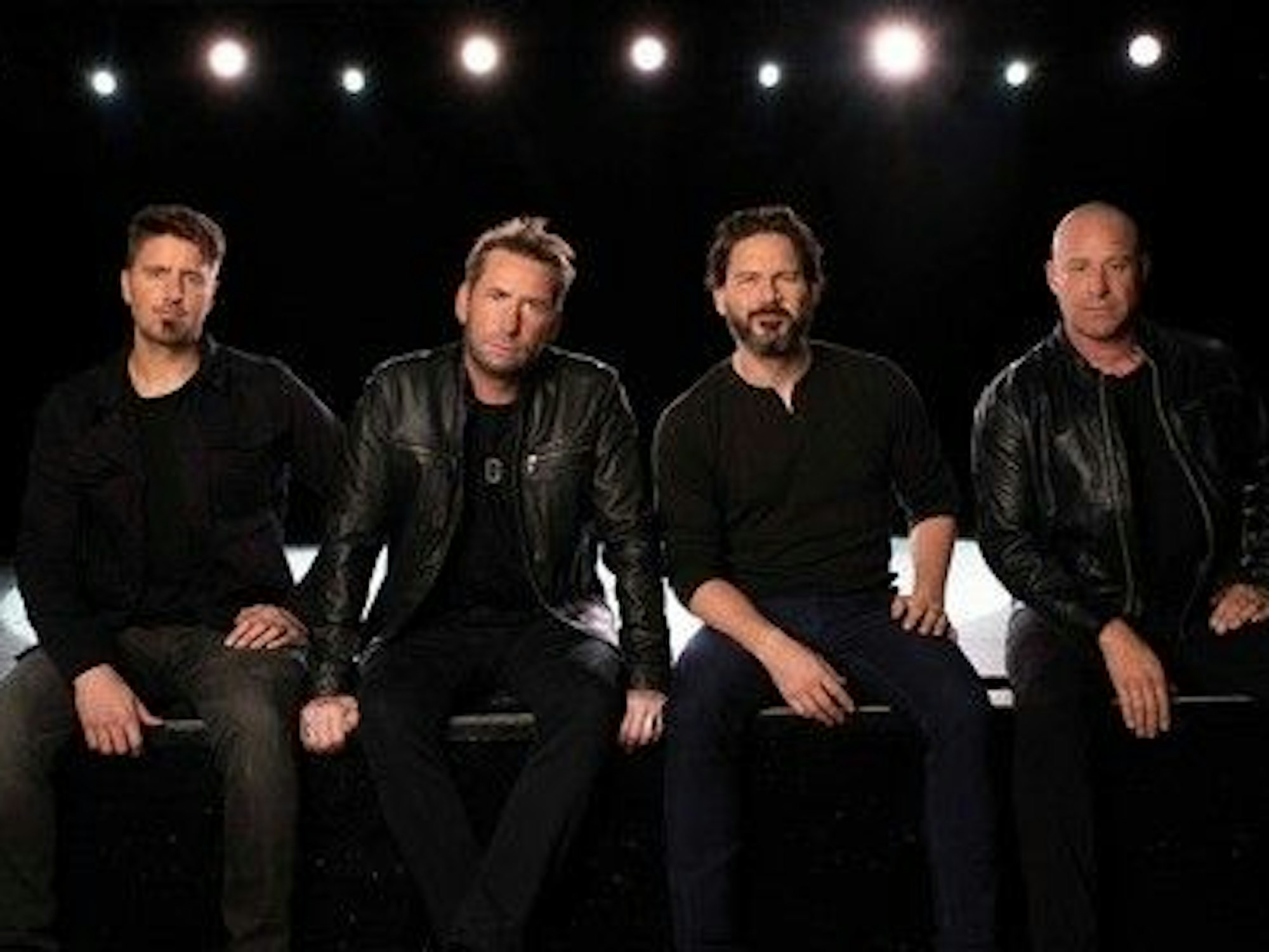 Die Band Nickelback sitzt in schwarzen Klamotten vor der Kamera.