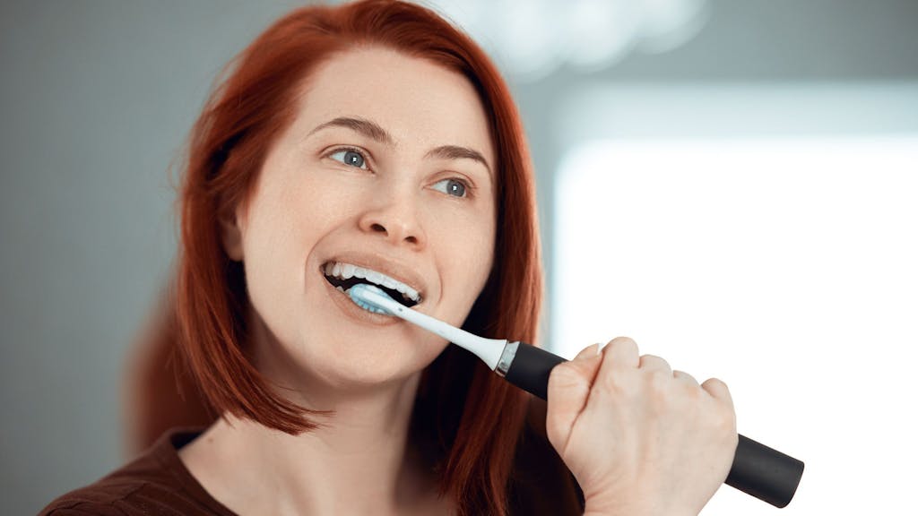 Auf dem Foto putzt sich eine rothaarige Frau die Zähne mit einer elektrischen Zahnbürste.