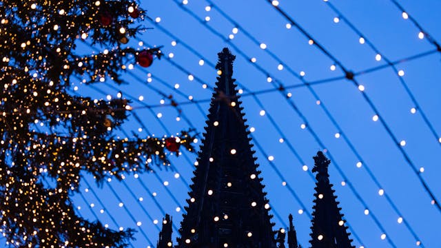 Spitzen des Kölner Doms sind hinter der Beleuchtung des Weihnachtsmarkts auf dem Roncalliplatz zu sehen