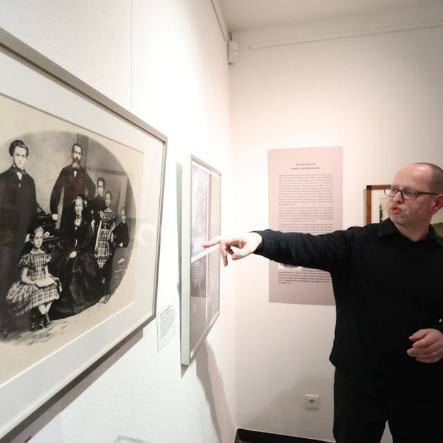Ein Mann zeigt auf ein historisches Schwarz-Weiß-Foto, das die Familie von „Wolfgang Müller von Königswinter“ zeigt.