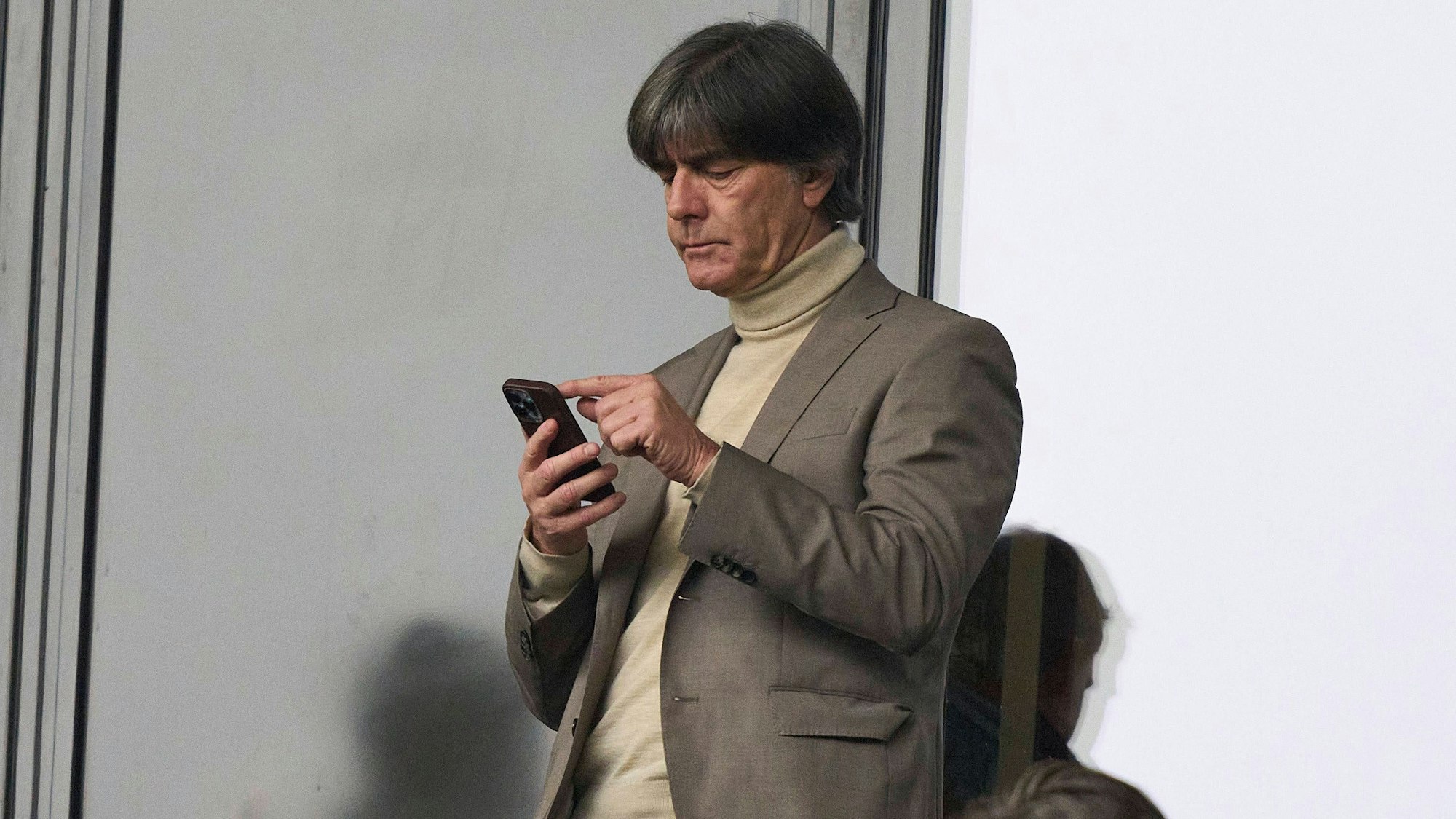 Joachim Löw blickt im Stadion auf sein Handy.