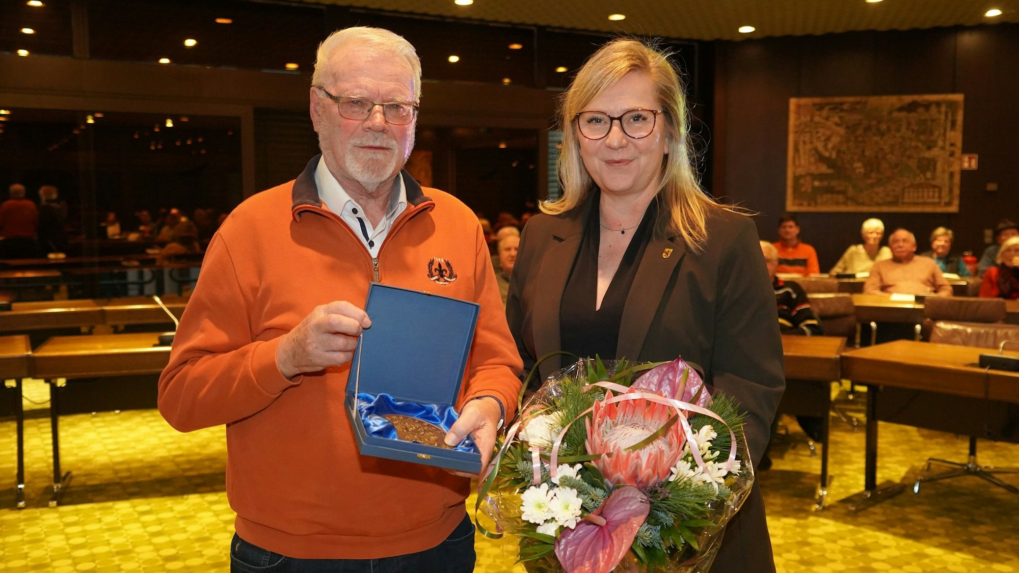 Das Foto zeigt Peter Kleinen und Frechens Bürgermeisterin Susanne Stupp. In den Händen hält er die Ehrengabe der Stadt Frechen, sie einen Blumenstrauß.
