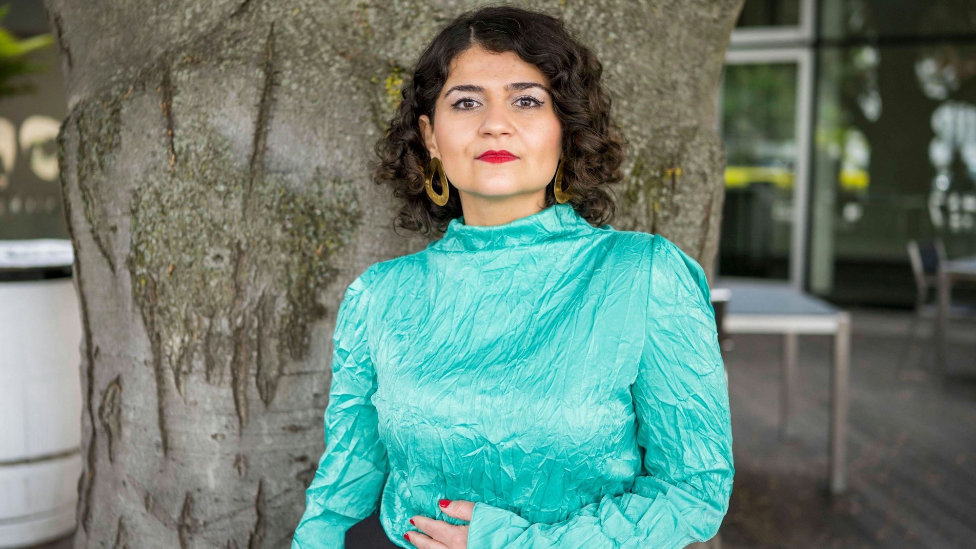 Die Regisseurin Pınar Karabulut posiert vor einem Baumstamm. Sie trägt eine türkis-schimmernde Bluse.